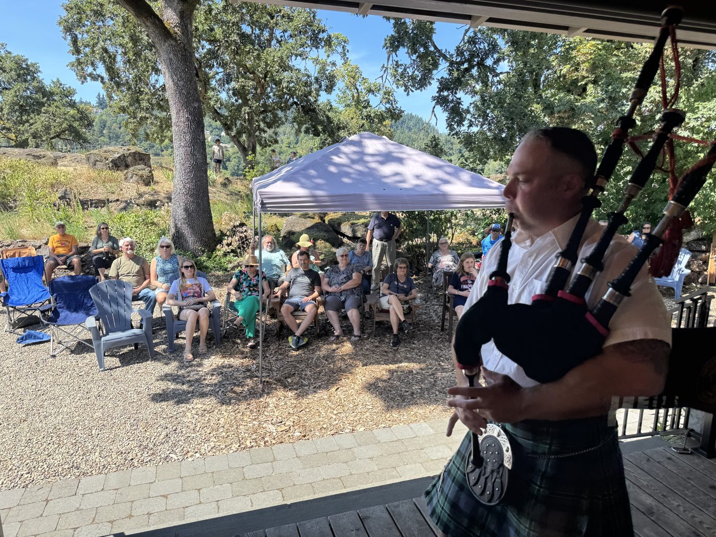 A bagpiper performing for a seated crowd under shade tents